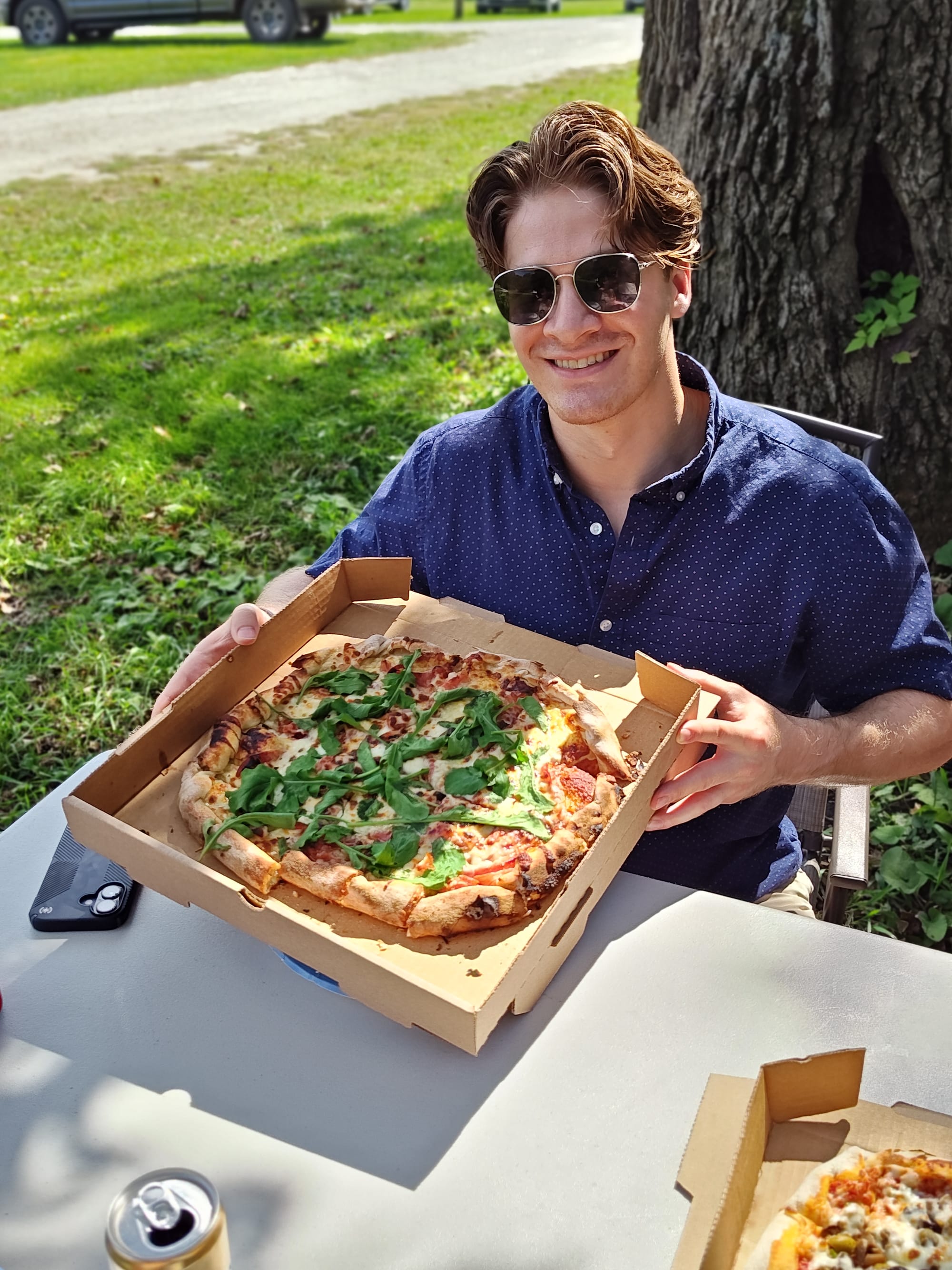smiling man holding a whole, sweet pizza