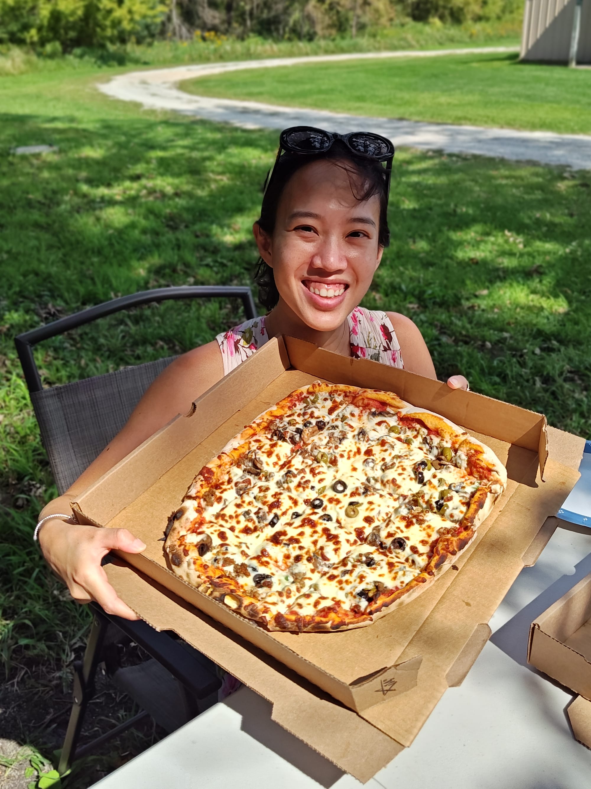 smiling woman holding a whole, meat and olive pizza