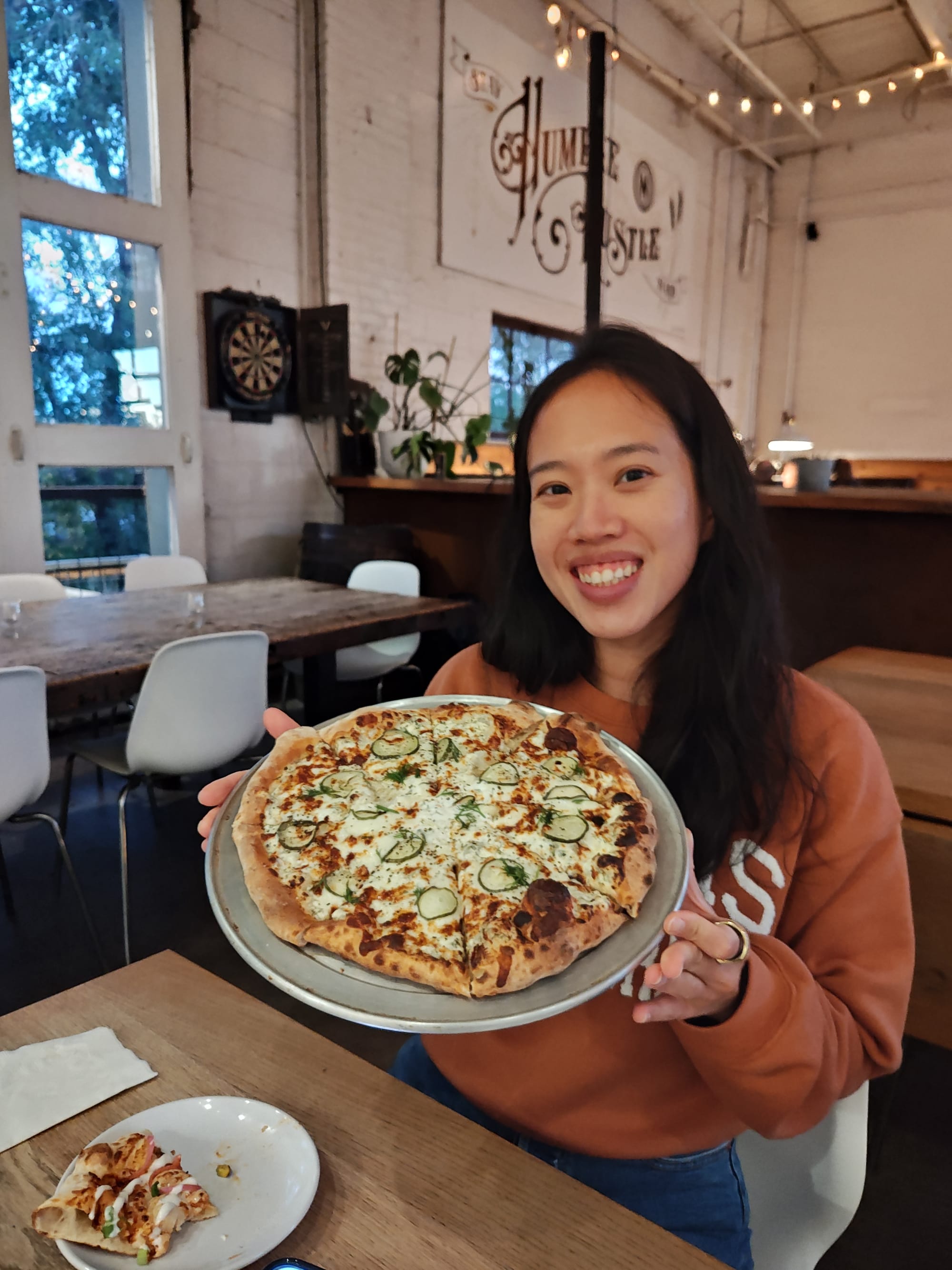 smiling woman holding a pickle pizza